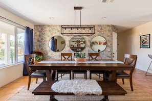 Un coin repas avec une table en bois, quatre chaises, un tapis blanc et moelleux, et un mur orné de trois miroirs ronds et d’un luminaire suspendu.