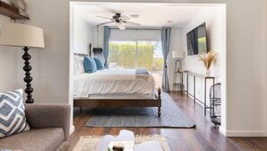 A bedroom with a bed, a ceiling fan, a window with curtains, a TV, and a small table with a lamp. - Casa Bermuda a Spanish Boho Retreat, Expansive Pool/Spa Pet Friendly (Bermuda Dunes)