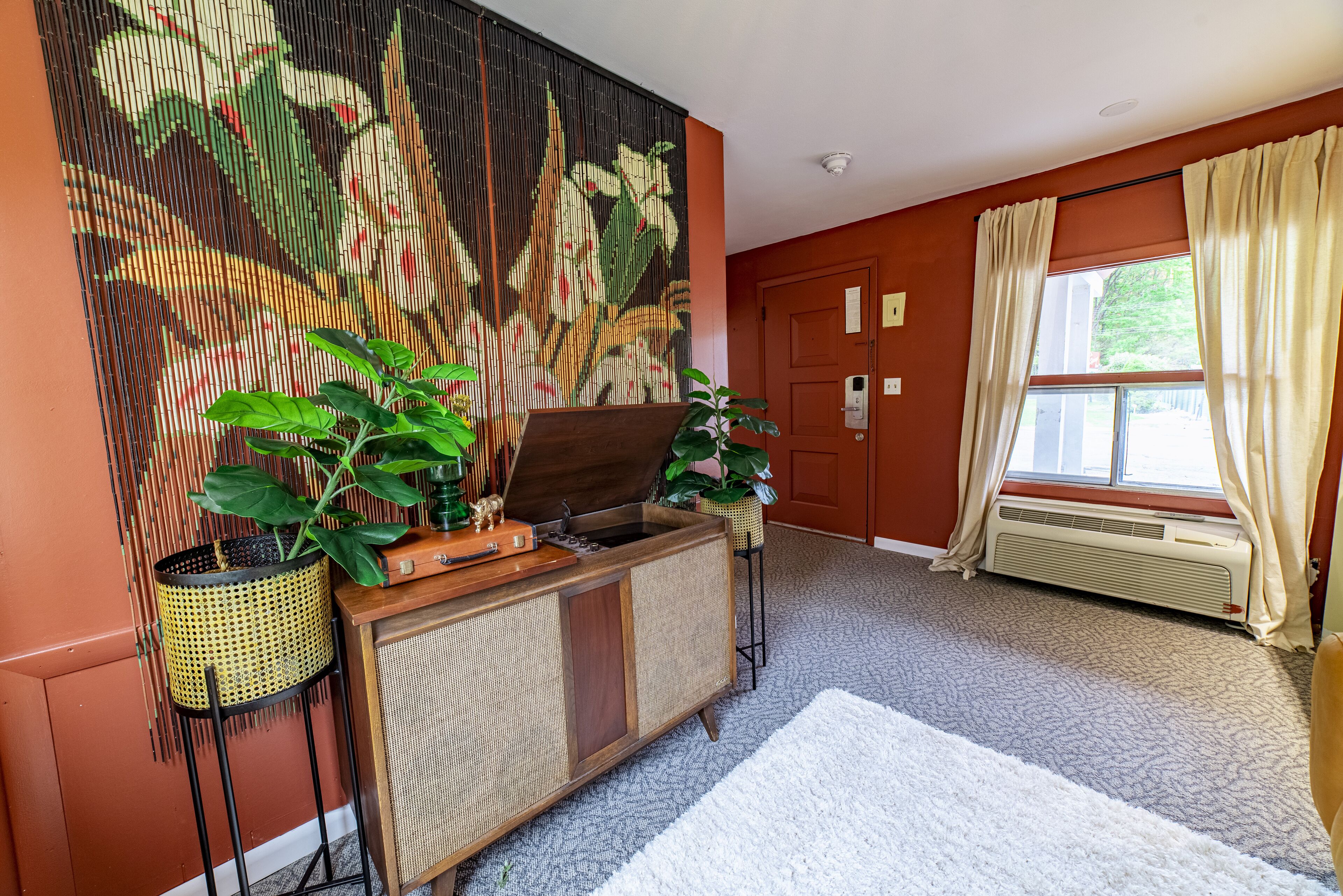 A room with a large woven tapestry, a wooden cabinet with a sink, a radiator, and a window with curtains.