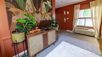 A room with a large woven tapestry, a wooden cabinet with a sink, a radiator, and a window with curtains.