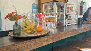 Eine Bar mit Hockern und einer Theke, auf der Früchte und Getränke präsentiert werden, sowie ein Schild mit der Aufschrift 'Springs'.