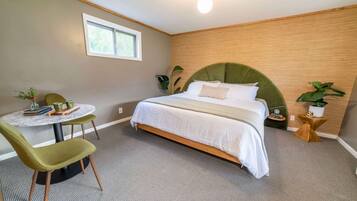 A bedroom with a bed, a round table with chairs, a window, and a plant.