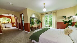 Ein Hotelzimmer mit einem großen Bett, einem Schreibtisch, einem Sessel und Blick ins Freie.