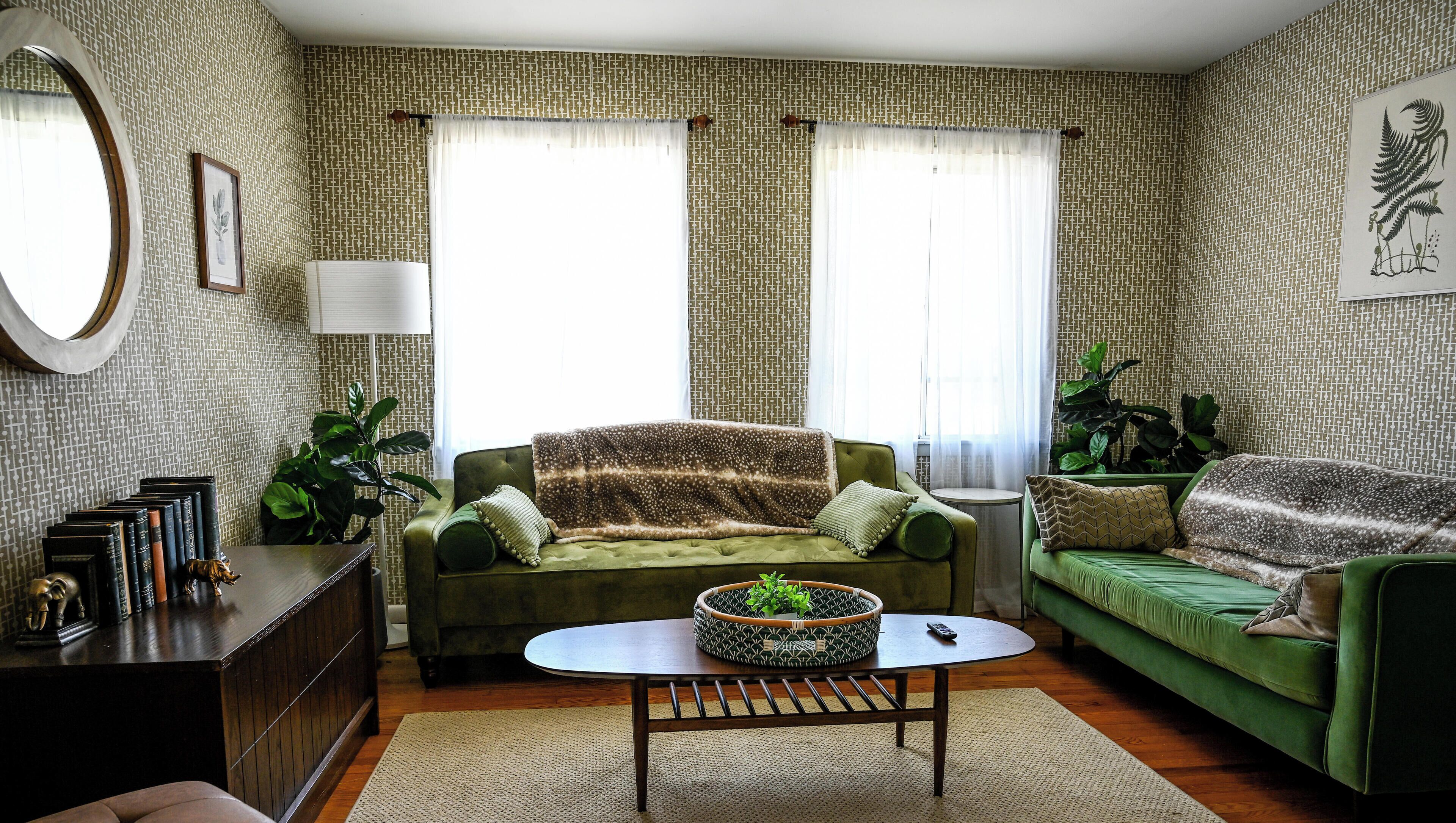 Een woonkamer met behang met patroon, twee groene banken, een salontafel en een bijzettafeltje.