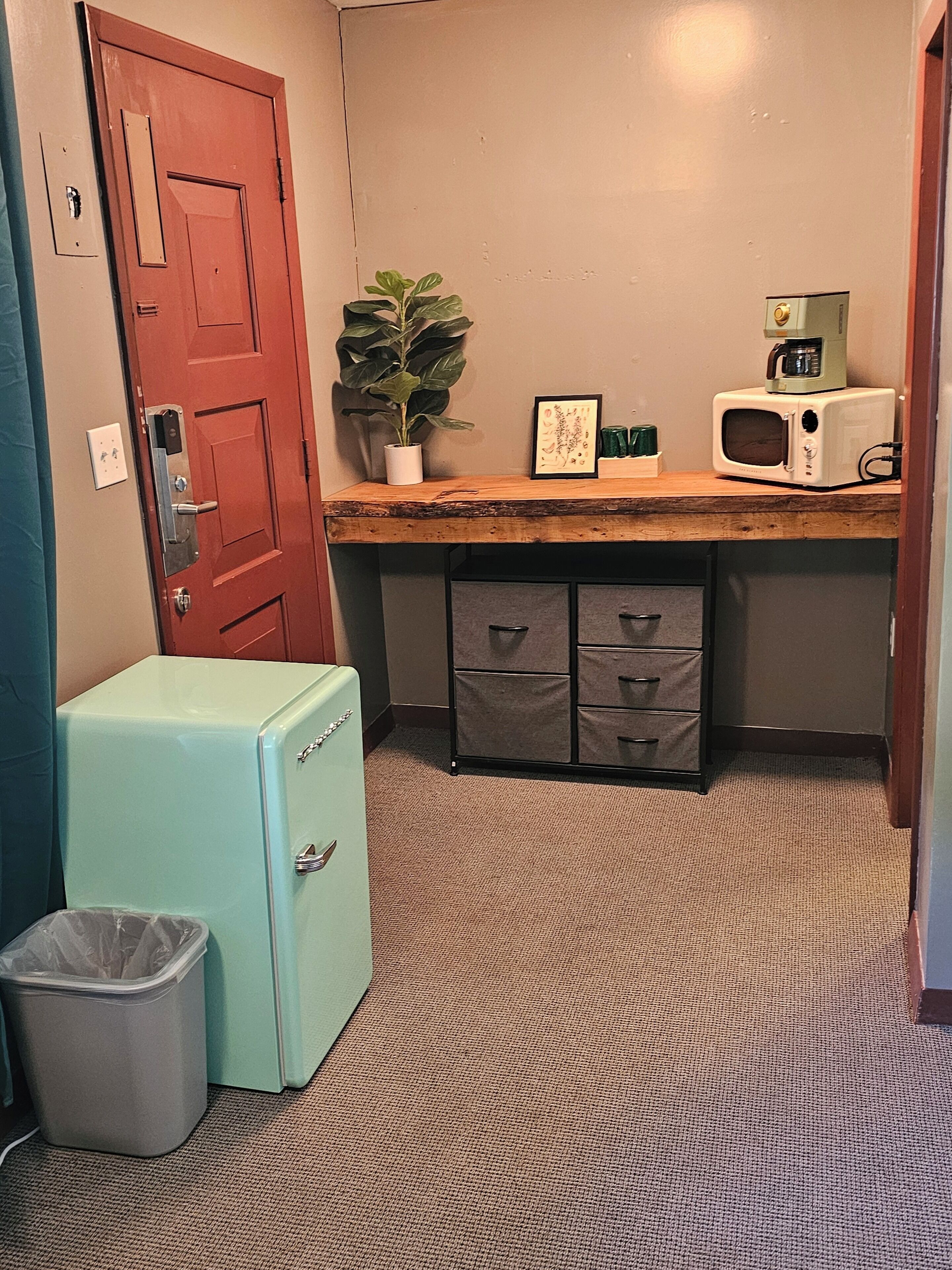 Una kitchenette compacta con un refrigerador antiguo, un microondas, una cafetera y una pequeña planta en maceta.