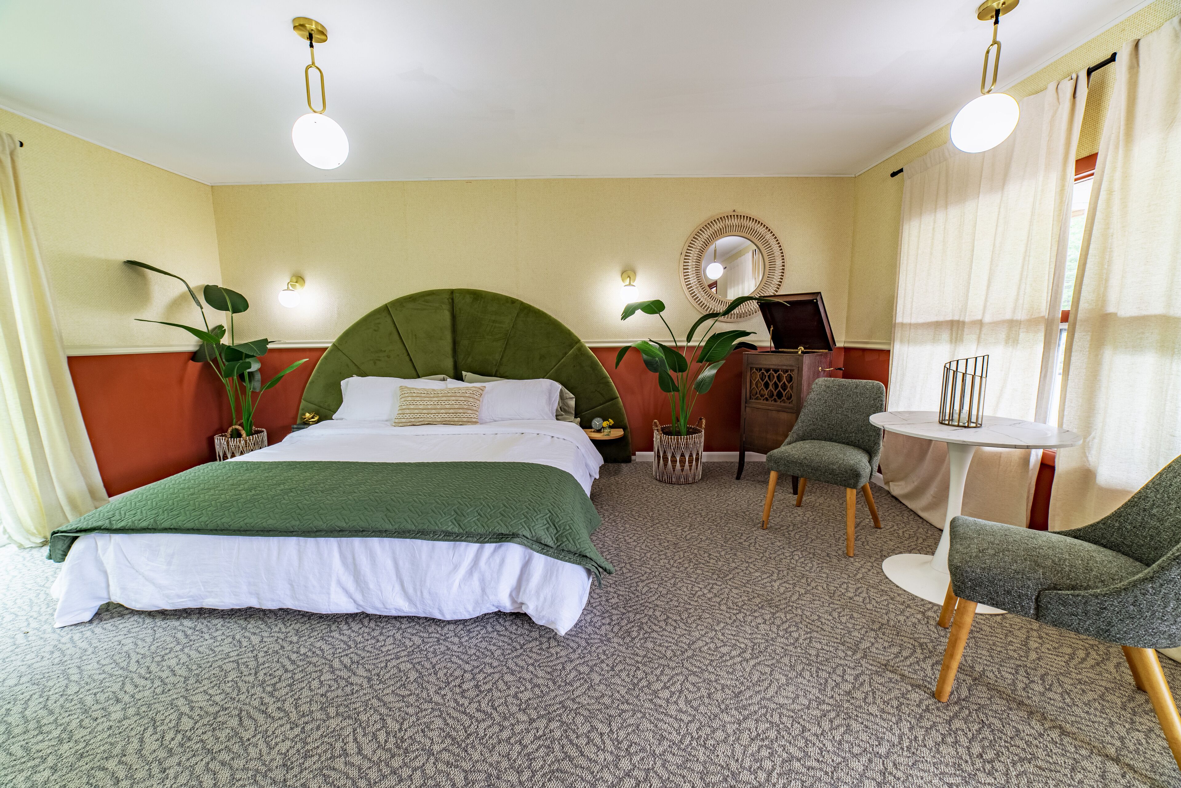 Una habitación de hotel con una cama grande, dos sillones, una mesita y dos plantas en macetas.