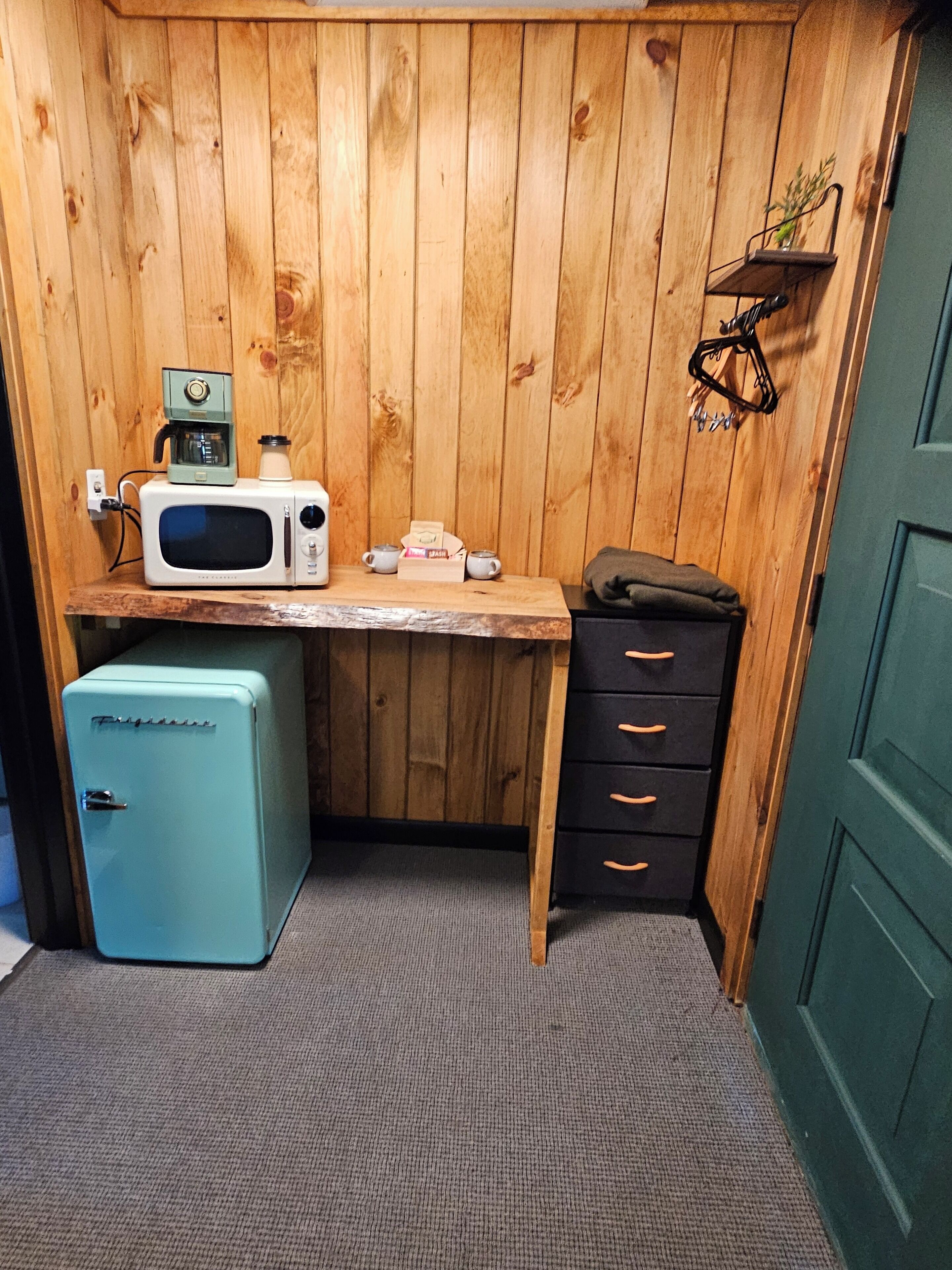 Una kitchenette compacta con microondas, cafetera y refrigerador pequeño.