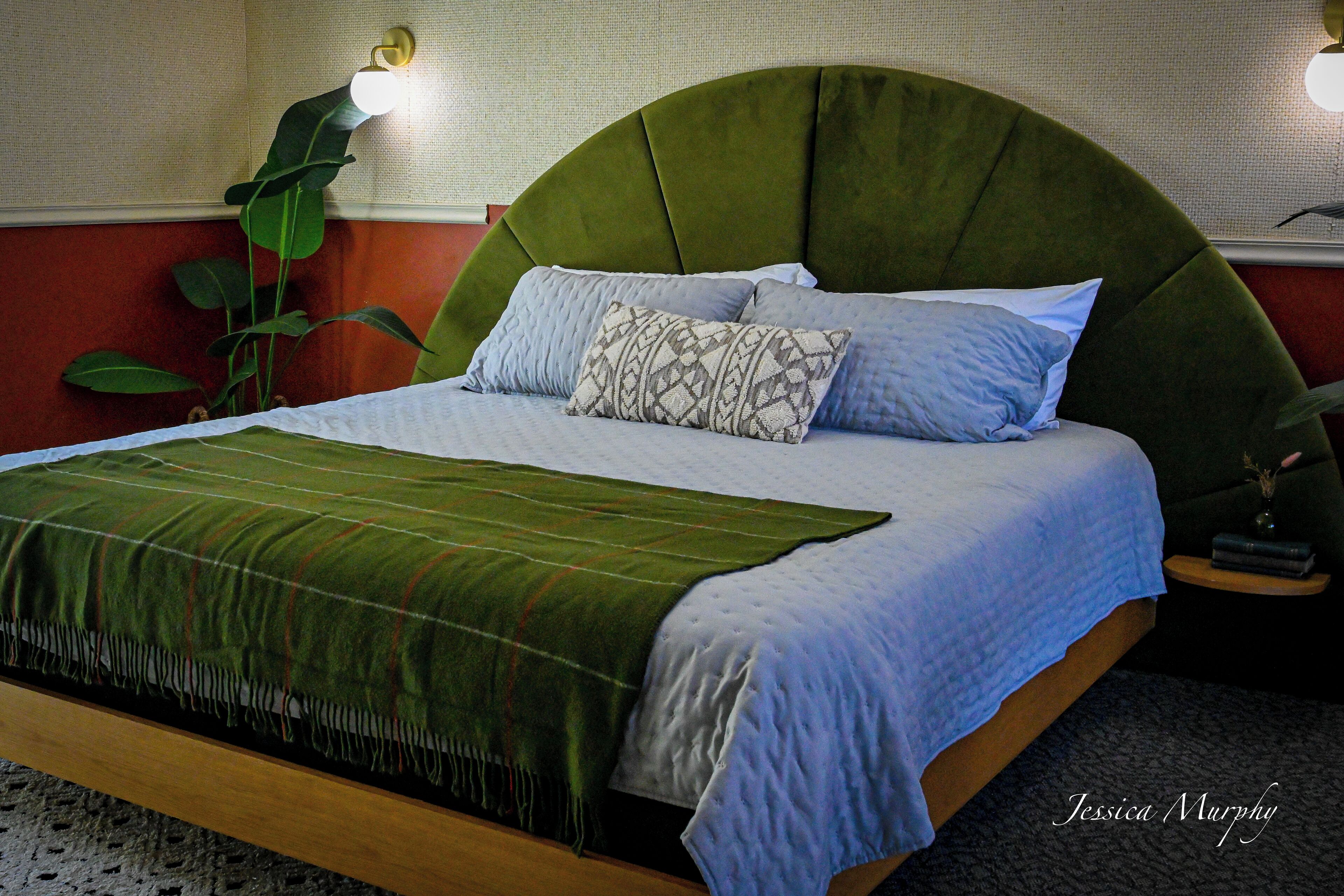 A bed with a green upholstered headboard, a patterned pillow, and a green blanket.