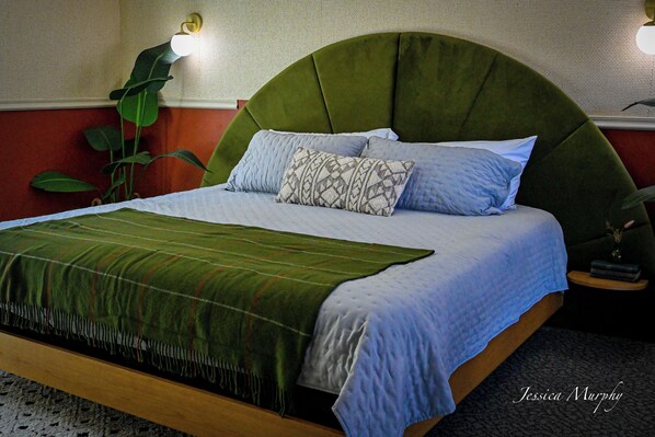 Een bed met een groen bekleden hoofdeinde, een gestreept kussen en een groene deken.