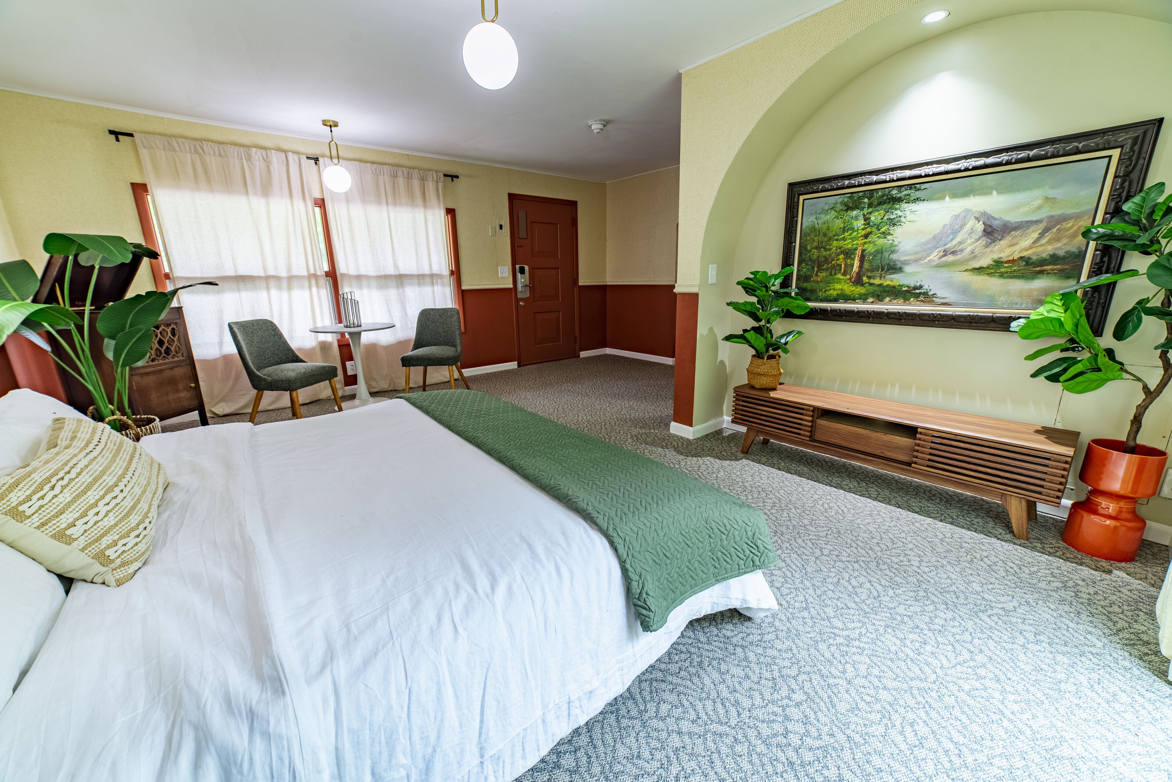 Ein Hotelzimmer mit einem Bett, einem Schreibtisch, einem Stuhl, einem Gemälde und Topfpflanzen.