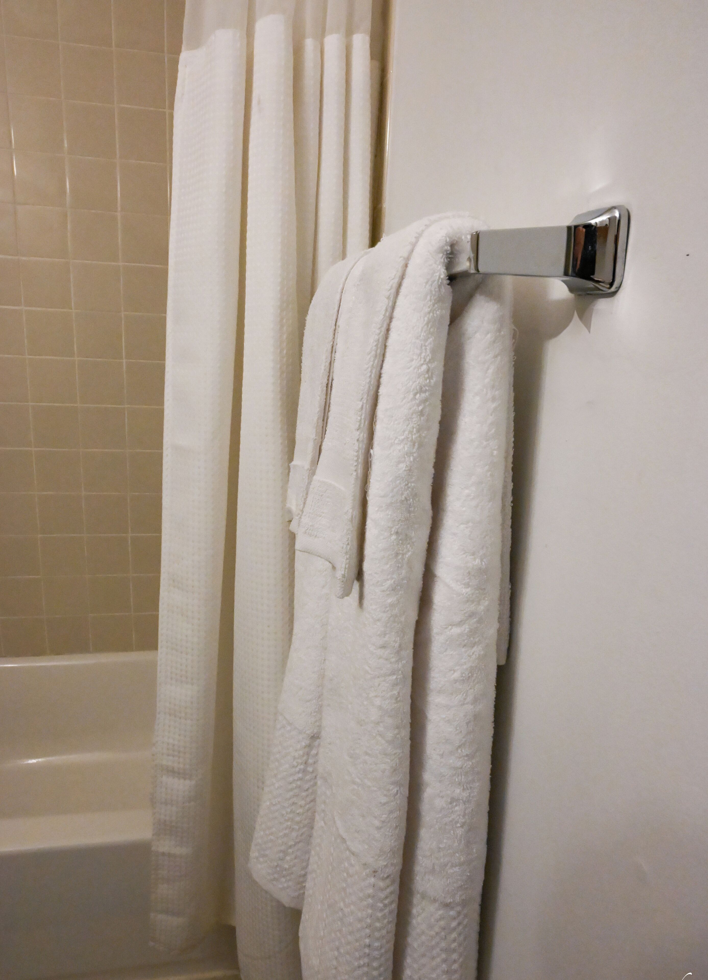 Un bagno con una vasca da bagno bianca, un portasciugamani bianco con due asciugamani e una tenda da doccia bianca.