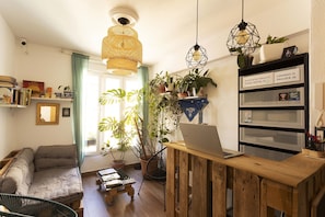 A cozy living room with a sofa, a wooden desk with a laptop, and a bookshelf.