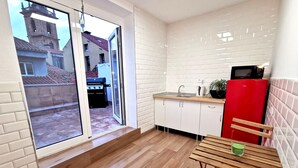 A modern kitchen with white cabinets, a red refrigerator, and a wooden dining table. - Green Hostel (Oviedo)