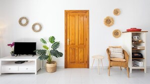 A room with a wooden door, a white TV stand, a potted plant, a wicker chair, and a white cabinet with shelves. - Home2Book Stylish Apt Pool & Terrace, Sand Club (Oasis del Sur)