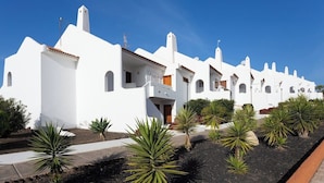 A row of white buildings with balconies, surrounded by landscaped areas with yucca plants. - Home2Book Stylish Apt Pool & Terrace, Sand Club (Oasis del Sur)
