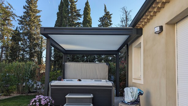A covered outdoor seating area with a bench, a hot tub, and a small table.