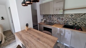A modern kitchen with a wooden table, hanging pendant lights, and a tiled backsplash.