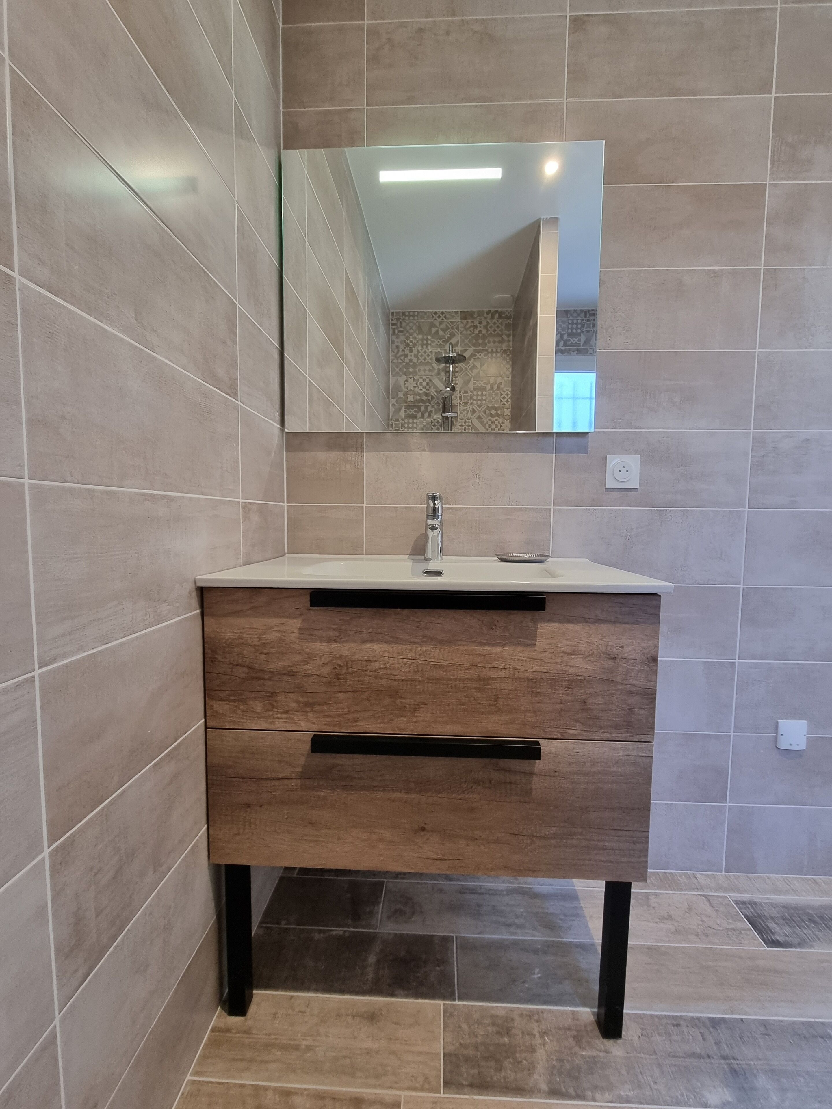 A bathroom with a modern vanity, a mirror, and a shower area.