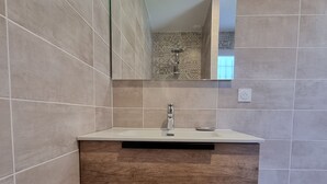 A bathroom with a modern vanity, a mirror, and a shower area.
