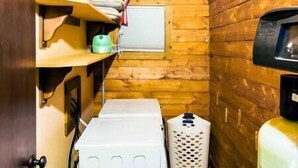 A compact bathroom with wooden walls, a white washing machine, a laundry basket, and a water heater.