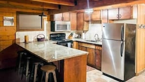 A kitchen with wooden cabinets, a stainless steel refrigerator, a microwave, and a granite countertop.