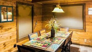 A wooden cabin interior with a dining table set for four, a vase with dried plants, and a hanging light fixture.