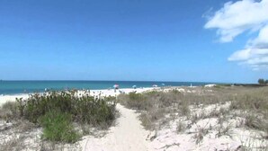 A beach path leading to the sea with umbrellas and beachgoers.