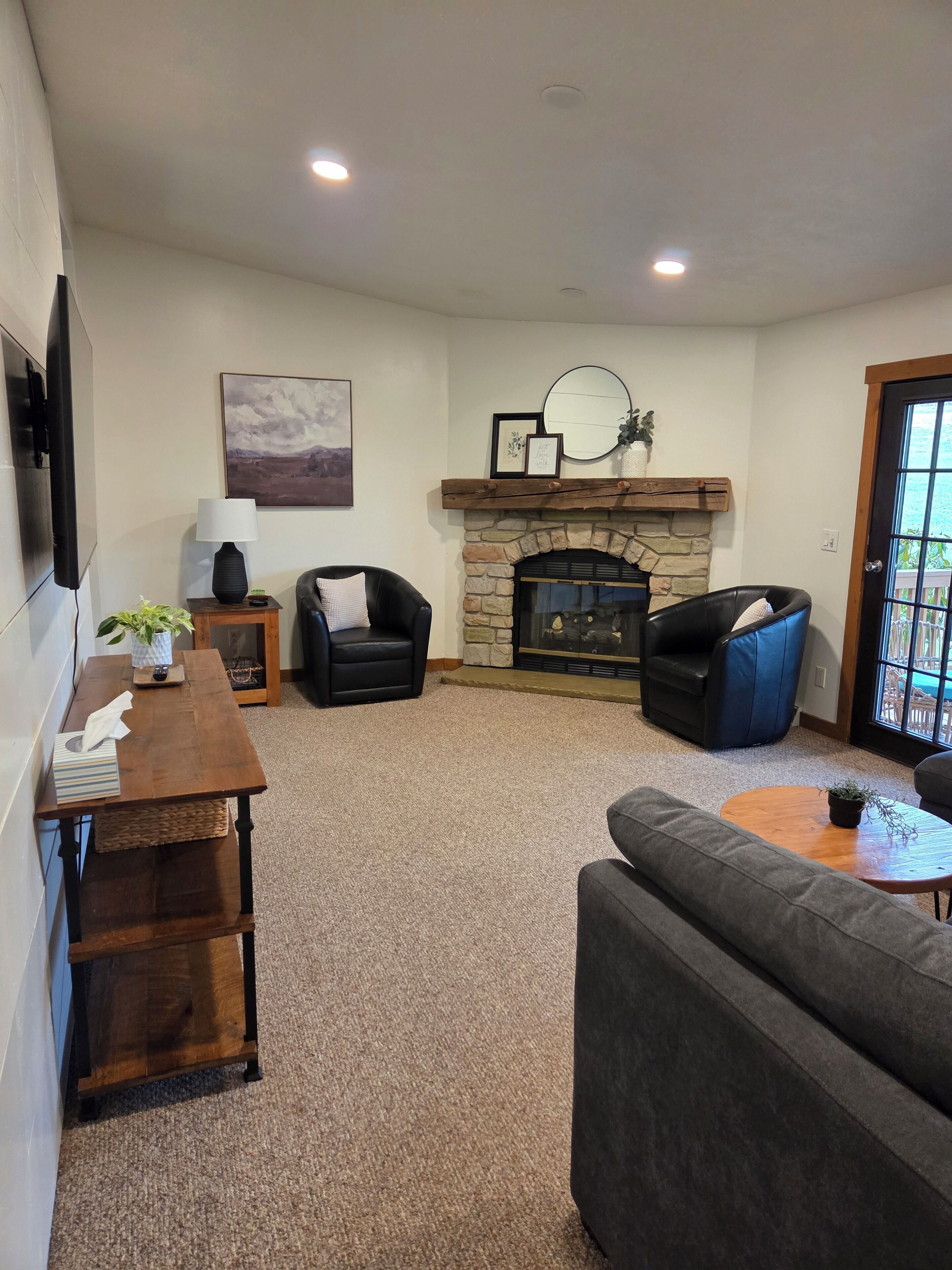 A living room with a stone fireplace, two black leather sofas, a wooden coffee table, and a television mounted on the wall.