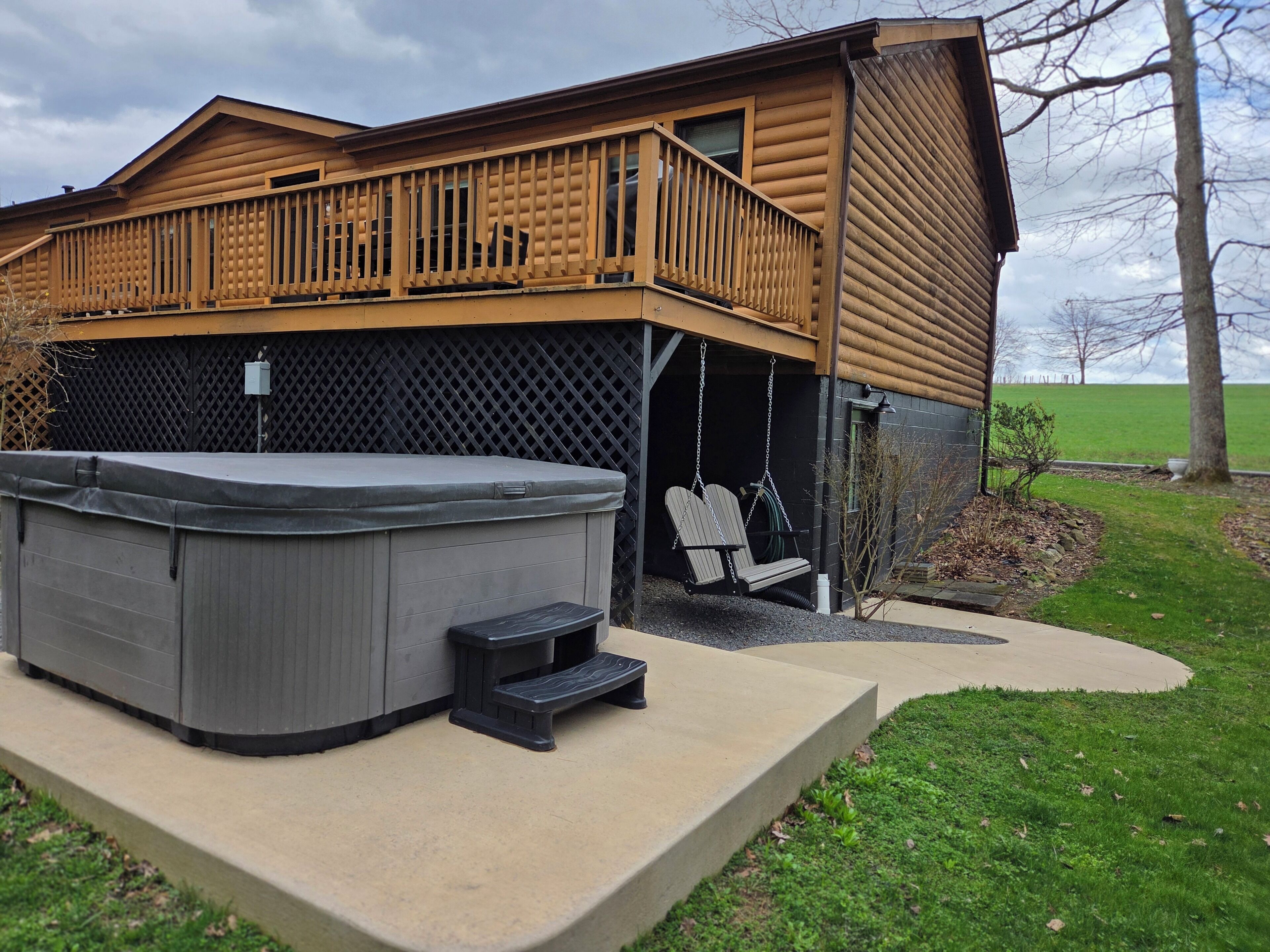 A wooden cabin with a hot tub and two swing chairs outside.