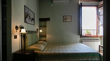 Un dormitorio con una cama, dos lámparas fijadas a la pared, un radiador y una ventana con vistas a la vegetación.