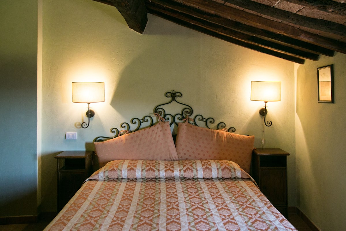 Une chambre à coucher avec une couvre-lit à motifs, deux lampes de chevet, une tête de lit en bois et une petite table de chevet de chaque côté du lit.