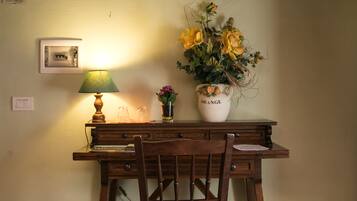 A wooden desk with a lamp, a vase with flowers, and a framed picture on the wall.