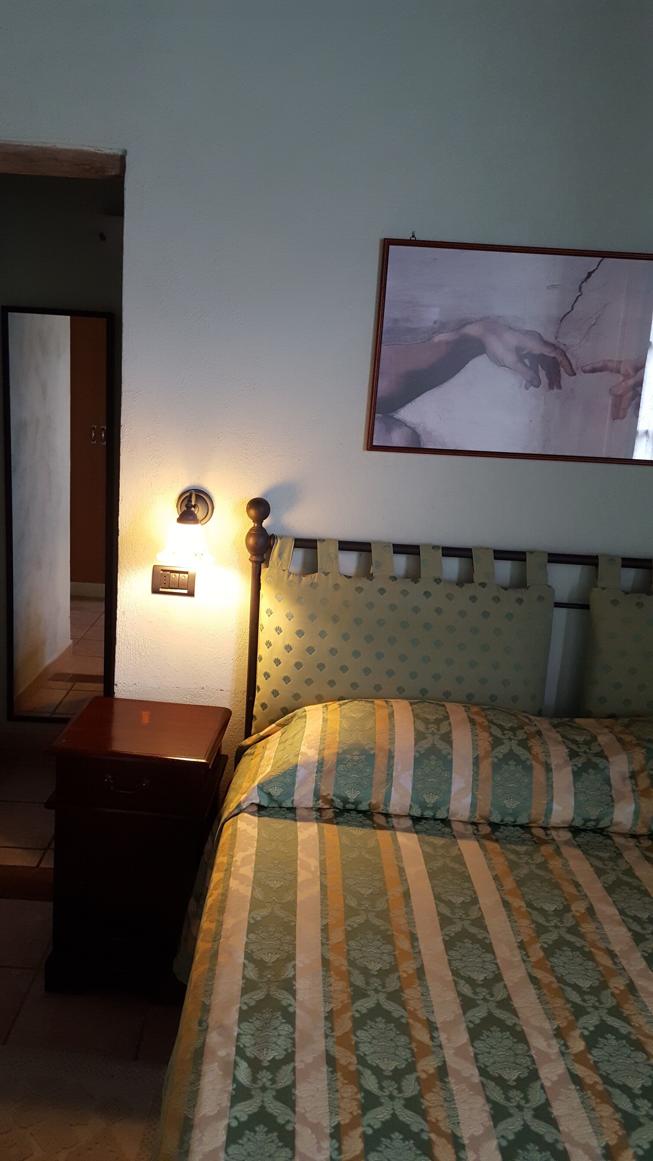 Un dormitorio con una cama, una mesita de noche, una lámpara de pared y un cuadro enmarcado.
