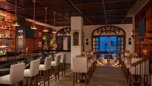 A bar area with a marble countertop, bar stools, and hanging pendant lights. There is a view of the ocean through an arched doorway. - Zoëtry Casa del Mar intimate, oceanfront luxury and golf (San José del Cabo)