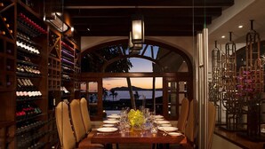 A dining area with a table set for six, surrounded by wooden chairs, with a view of the sunset and palm trees through an arched window. - Zoëtry Casa del Mar intimate, oceanfront luxury and golf (San José del Cabo)