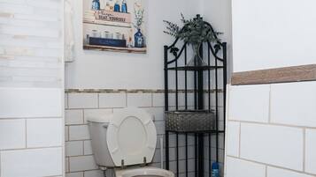 A bathroom with a toilet, a shelf with toiletries, and a decorative sign.