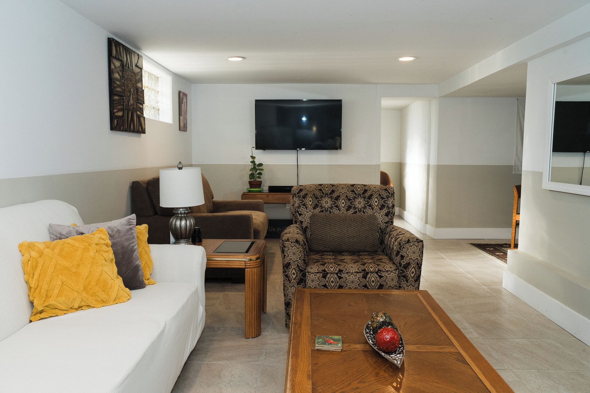 Un salon moderne comprenant un canapé, un fauteuil, une table basse et un téléviseur à écran plat fixé au mur.