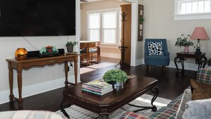Una sala de estar con una mesa de centro de madera oscura, un sillón azul, un sofá, un televisor y una estantería.