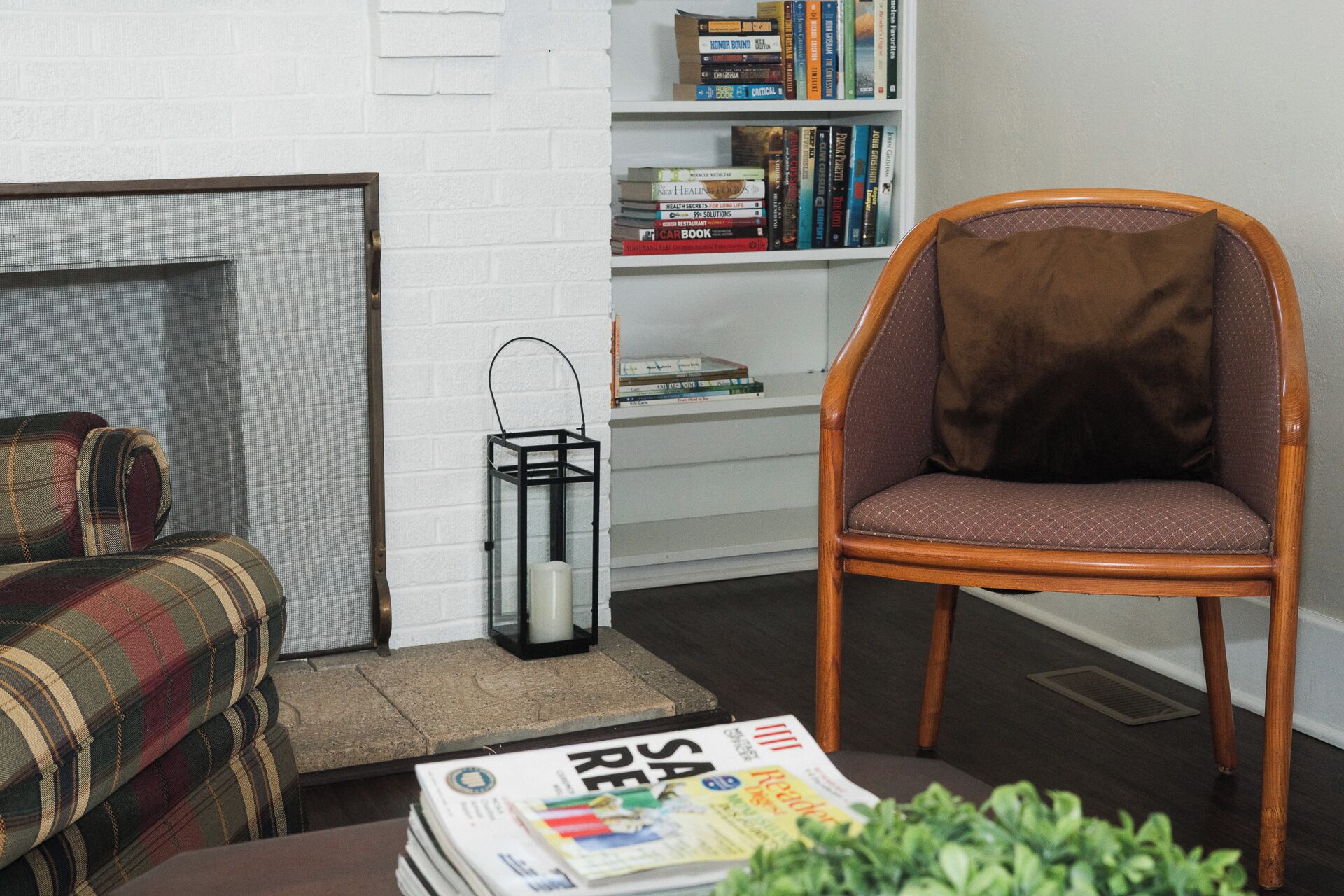 Een woonkamer met een geruite bank, een houten stoel, een boekenkast en een tijdschrift op de vloer.