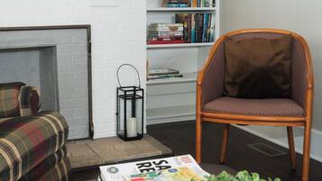 Een woonkamer met een geruite bank, een houten stoel, een boekenkast en een tijdschrift op de vloer.