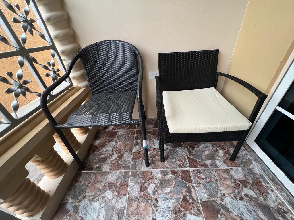 Ein Balkon mit zwei Korbstühlen und einer kleinen Couch, einem Fliesenboden und einem dekorativen Metallgitter.