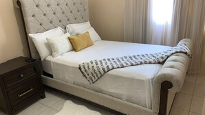 Een net opgemaakt bed met een gestoffeerd hoofdbord, een witte dekbedovertrek en een geborduurde deken.