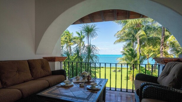A balcony with a view of the ocean, furnished with a sofa and a table set for tea. - Villa del Sol | 6BR | Exclusive Family Retreat (Cancún)