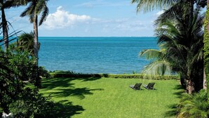 A grassy lawn with two lounge chairs facing a beach with clear blue water and palm trees. - Villa del Sol | 6BR | Exclusive Family Retreat (Cancún)