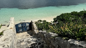 A coastal view with a clear turquoise sea, a stone wall, and some vegetation. - Villa del Sol | 6BR | Exclusive Family Retreat (Cancún)