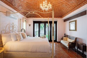 A hotel room with a large bed, a sitting area with a sofa, a chandelier, and a view of the outdoors. - Villa del Sol | 6BR | Exclusive Family Retreat (Cancún)