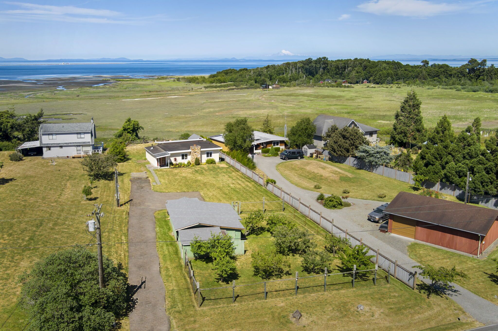 An aerial view of a residential area with houses, a fenced yard, and a clear view of the ocean.