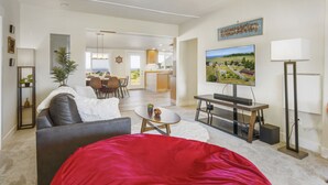 A modern living room with a red bean bag, a flat-screen TV, and a dining area in the background. - Experience Sequim Charm & Amazing Lighthouse Views, by the Olympic National Park (Sequim)