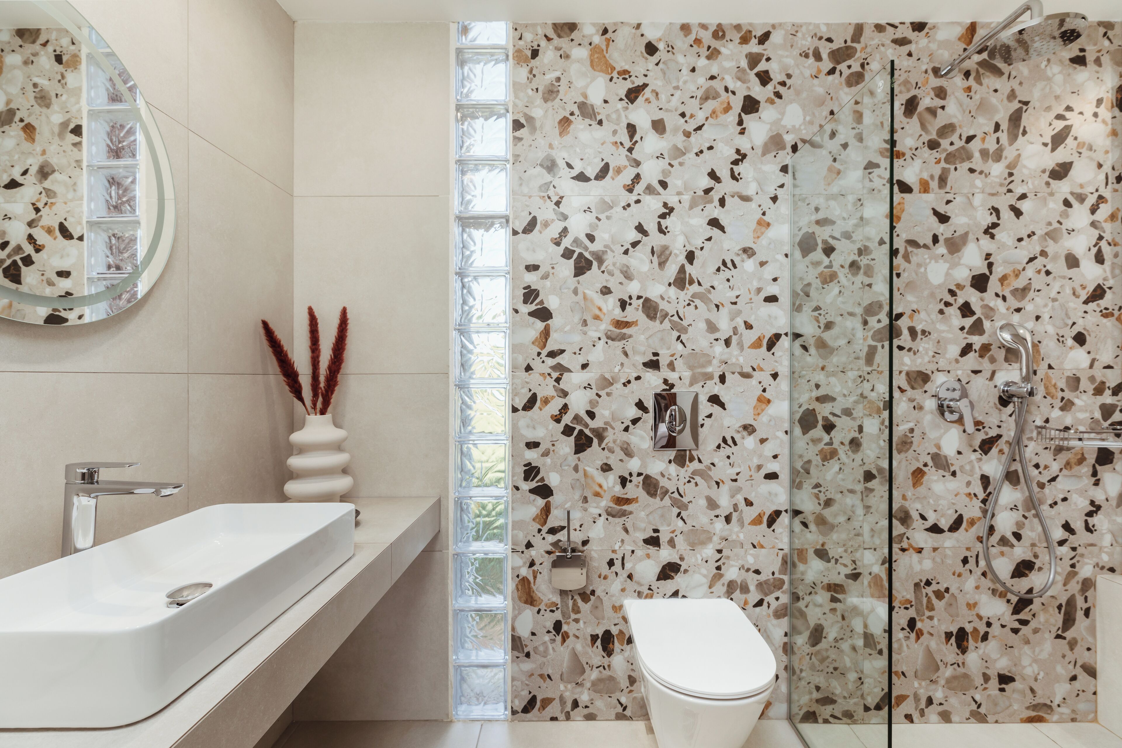 A modern bathroom with a white sink, a toilet, and a shower with a terrazzo tile wall.