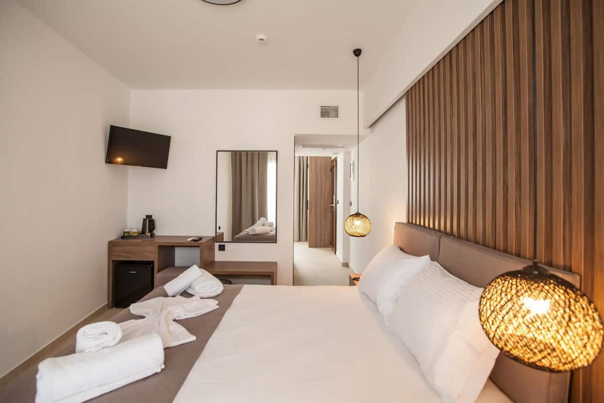 Habitación de hotel con una cama grande, un escritorio, un televisor de pantalla plana, un espejo y una lámpara de pared.